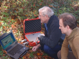 Zwei Geologen begutachten auf einem Outdoor-Laptop die Messgrafik im Gelände.