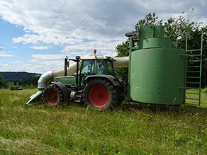 Ein Landwirt saugt mit einem am Traktor montierten Gerät Samen aus einer Wiese.