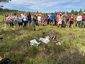 Menschgruppe steht auf einer Moorfläche, im Hintergrund Wald 