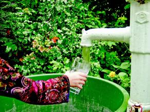 Eine Frau füllt ein Wasserglas an einer Pumpe auf