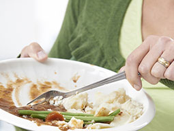 Eine Frau schiebt mit einer Gabel Essensreste von einem Teller.