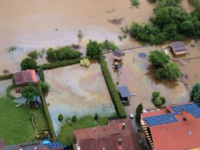 Luftbild einer Hochwassersituation in einem Siedlungsbereich. In den Vorgärten der Häuser steht Wasser, das durch Heizöl verunreinigt ist
