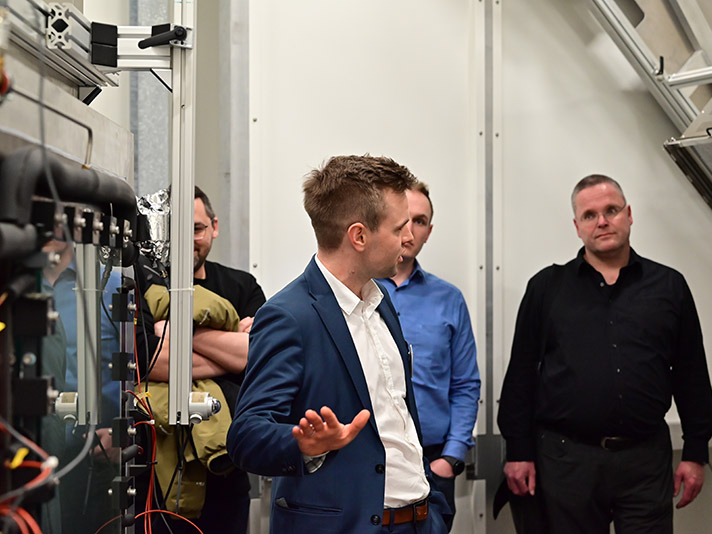 Teilnehmer einer Laborführung neben einer Wärmepumpe in einer Klimakammer