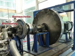 Auf dem Bild sieht man den Aufbau des Bremsenprüfstandes der Universität Bayreuth. Die Anlage besteht aus einer Bremsscheibe mit Bremsbelägen und einem Schwungrad, mit dem die Energie eines sich bewegenden Fahrzeuges simuliert werden kann. Der Bremsvorgang wird über ein Computerprogramm gesteuert.