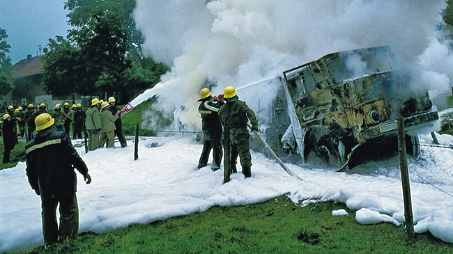 Ausgebrannter Lastwagen, umhüllt von weißem Löschschaum, der noch von der Feuerwehr aufgebracht wird