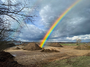 Auf einer Fläche wurde Oberboden zu Mieten zusammengeschoben, darüber spannt sich ein Regenbogen.