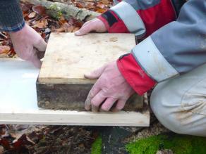 9. Mitarbeiter drücken eine Bodenziegel mithilfe einer Holzplatte vom Stahlrahmen auf die Trägerplatte mit Weißleim.