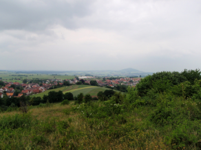 Hügelige, Vordere Rhön im Sandstein des Buntsandsteins mit einem spitzen Vulkankegel aus Basalt im Hintergrund.