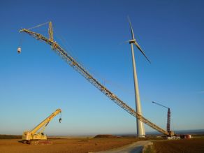 Ein Hochbaukran wird nach Vollendung der nebenan stehenden Windenergieanlage abgesenkt, um für den Rücktransport zerlegt zu werden.