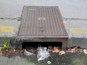 Kunststoffabfall und Reifenabrieb am Straßenrand neben einem Straßenabfluss. Das Mikroplastik gelangt so über das Abwassersystem in unsere Böden.