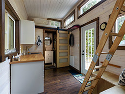 Tiny House mit Küche und Bad. Eine Leiter führt auf die Schlafempore
