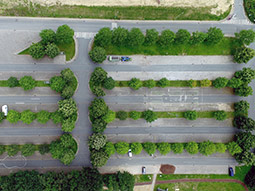 Parkplatz aus der Vogelperspektive: einzelne Autos, Bäume zwischen den Parkreihen, sehr viel Asphalt.