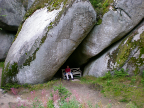 Person auf einer Ruhebank in einer Nische unter den riesigen Felsen der Luisenburg-Felsformation.