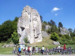 Am großen Burgsteinfelsen steht eine Gruppe Radfahrer vor der Infotafel