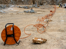 Aufgerollte tragbare Kabeltrommel mit kleinen Metallmessstäben auf der Steinbruchsohle