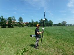 Der Geologe auf einer Wiese hält den ca. drei Meter langen Messstab und trägt die Messinstrumente.