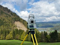 Tachymeter, im Hintergrund Rutschung in bewaldetem Hang