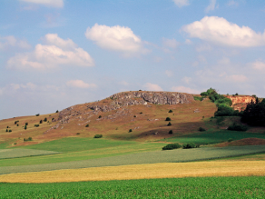 Begrünter Hügel unter weiß-blauem Himmel.