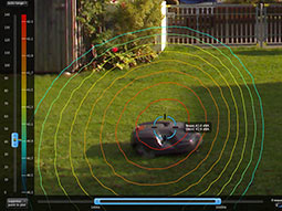 Ein Mähroboter fährt auf dem Rasen. Zur Veranschaulichung der Geräuschbildung sind Isophone abgebildet