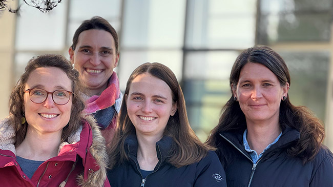 Vier junge Frauen stehen im Freien vor der Glasfassade.