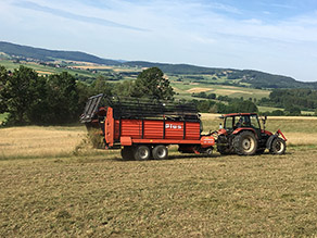 Mähgut wird mit einem Ladewagen auf eine Wiese aufgebracht.