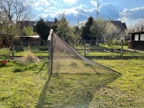 Eine zeltartig aussehende, nach links ausgerichtete Malaisefalle steht auf einer Wiese eines Hausgartens.