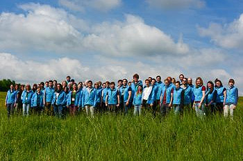 Gruppenbild von Menschen mit hellblauen Jacken, die auf einer Wiese stehen.