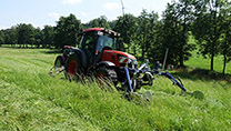 ein Traktor mäht eine Wiese, im Hintergrund eine Baumreihe ein Traktor mäht eine Wiese, im Hintergrund eine Baumreihe