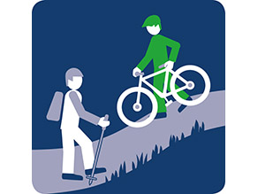 Ein Mensch auf Pfad begegnet einem Menschen, der ein Fahrrad schiebt.