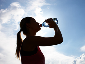 Frau trinkt aus Wasserflasche bei strahlendem Sonnenschein.