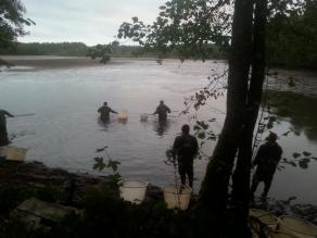 Mehrere Männer in Wathosen und mit Kescher in der Hand in einem Teich, dessen Wasserspiegel stark gesunken ist. Sie fischen Karpfen ab.