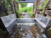 PM 32/2025:  Zur Krebssperre umgebauter Sohlabsturz in Freyung-Grafenau. Alle rauen und vormals kletterbaren Teile wurden mit glatten und überstehenden Blechen umkleidet, sodass das Bauwerk von Flusskrebsen nicht länger überwunden werden kann. 