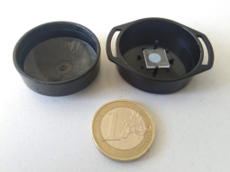 Schwarze, runde Kunststoffdose mit Detektor, insgesamt nur wenig größer als eine Ein-Euro-Münze.