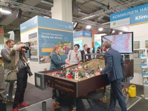 Das Foto zeigt eine Gesprächssituation mit Staatsminister Thorsten Glauber bei dem am Stand ausgestellten Naturgefahrenmodell des WWA Rosenheim.