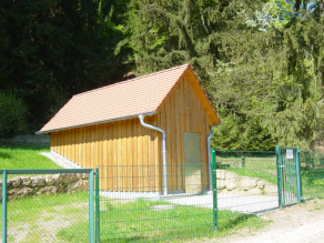Kleines Holzhaus im eingezäunten Fassungsbereich.