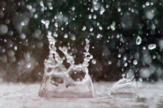 Ein großer Wassertropfen schlägt spritzend auf eine Wasseroberfläche.