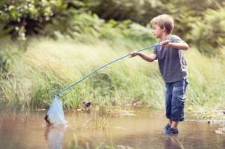 Ein kleiner Junge steht im Wasser und fischt mit einem Cacher.