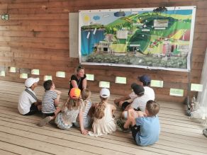 Eine Mitarbeiterin der Regierung der Oberpfalz sitzt mit einer Gruppe Kinder am Boden und erklärt das Trinkwasserversorgungsmodell. Das Modell hängt im Hintergrund an der Wand, verschiedene Schläuche und Kammern verdeutlichen den Weg des Trinkwassers von der Quelle bis zu uns nach Hause. Eine Mitarbeiterin der Regierung der Oberpfalz sitzt mit einer Gruppe Kinder am Boden und erklärt das Trinkwasserversorgungsmodell. Das Modell hängt im Hintergrund an der Wand, verschiedene Schläuche und Kammern verdeutlichen den Weg des Trinkwassers von der Quelle bis zu uns nach Hause.