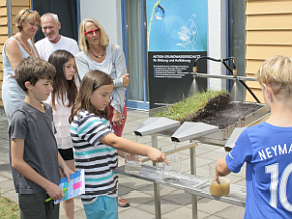 Schulkinder vor einem Versuchsaufbau zum Abfluss von Wasser.