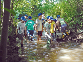 Schulkinder waten in einem seichten Bach umher.