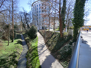 Blick von einer Brücke auf den Bach ohne Breitenvarianz. Ein Geh- und Radweg verläuft parallel dazu.