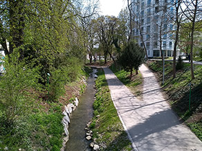 Blick von einer Brücke auf einen Bach und einen parallel verlaufenden Geh- und Radweg.