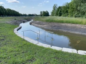 Eine Kneippmöglichkeit im neuen Seitenarm. Das Ufer ist mit Natursteinquadern gesichert. Eine Treppe mit Geländer führt in das Wasser. Ein rundlaufendes Geländer steht im Wasser.