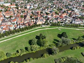 Luftaufnahme der Altmühl vor Maßnahmenumsetzung: Der Gewässerlauf ist monoton, geradlinig und ohne erkennbare Breiten- oder Strömungsvarianz. Die Ufer sind überwiegend dicht mit Gehölzen bewachsen. Zwischen der Innenstadt und dem Fluss befindet sich eine Grünfläche.