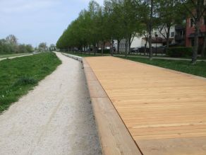 Ein Sonnendeck aus Holz auf einem Abschnitt der Hochwasserschutzmauer lädt zum Verweilen ein. Ein Weg führt entlang der niedrigen Mauer.
