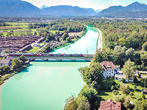 Luftaufnahme der Saalach im Bereich des Hochwasserschutz Freilassing (flussaufwärts): Blick auf eine Eisenbahnbrücke über die Saalach. Daneben überwiegend bewaldete Gebiete. Im Hintergrund die Berchtesgadener Alpen sowie die Chiemgauer Alpen mit dem Hochstaufen. Luftaufnahme der Saalach im Bereich des Hochwasserschutz Freilassing (flussaufwärts): Blick auf eine Eisenbahnbrücke über die Saalach. Daneben überwiegend bewaldete Gebiete. Im Hintergrund die Berchtesgadener Alpen sowie die Chiemgauer Alpen mit dem Hochstaufen.