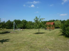 Eine Grünfläche mit jungen Obstbäumen. Im Hintergrund Sitzmöglichkeiten und eine Holzhütte.