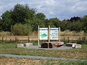 Zwei Infotafeln zum Wasserkreislauf und zu der Kahl stehen vor einem Holzgeländer. Davor einige Sitzmöglichkeiten aus Stein und ein Kiesweg. Zwei Infotafeln zum Wasserkreislauf und zu der Kahl stehen vor einem Holzgeländer. Davor einige Sitzmöglichkeiten aus Stein und ein Kiesweg.