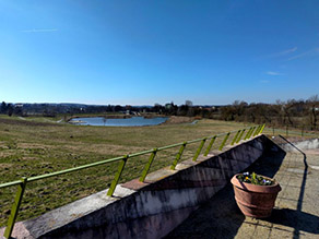 Blick über die Wilhelminenaue von einer Aussichtsplattform mit Geländer. Im Hintergrund die Grünanlage mit mehreren Wegen und ein Landschaftssee mit Seebühne. Blick über die Wilhelminenaue von einer Aussichtsplattform mit Geländer. Im Hintergrund die Grünanlage mit mehreren Wegen und ein Landschaftssee mit Seebühne.