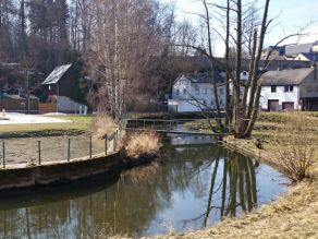 Ein strukturarmer Fluss mit Ufermauern zur Ufersicherung. Ein Steg führt über das Gewässer. Im Hintergrund Wohnbebauung. Ein strukturarmer Fluss mit Ufermauern zur Ufersicherung. Ein Steg führt über das Gewässer. Im Hintergrund Wohnbebauung.